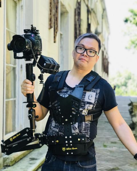 A color photograph of Simon CF Yu outside holding a camera