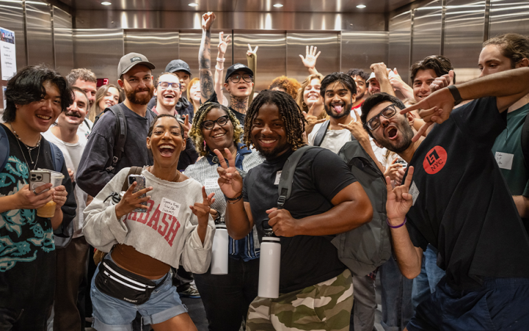 Group of students enthusiastically smiles at the camera with hands in the air