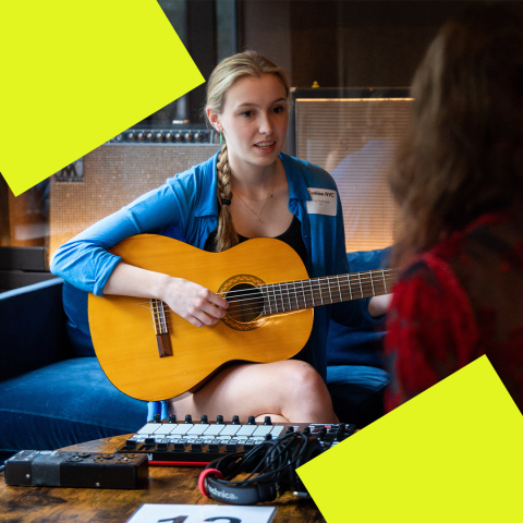 An S&P Student plays the guitar in front of a midi keyboard.